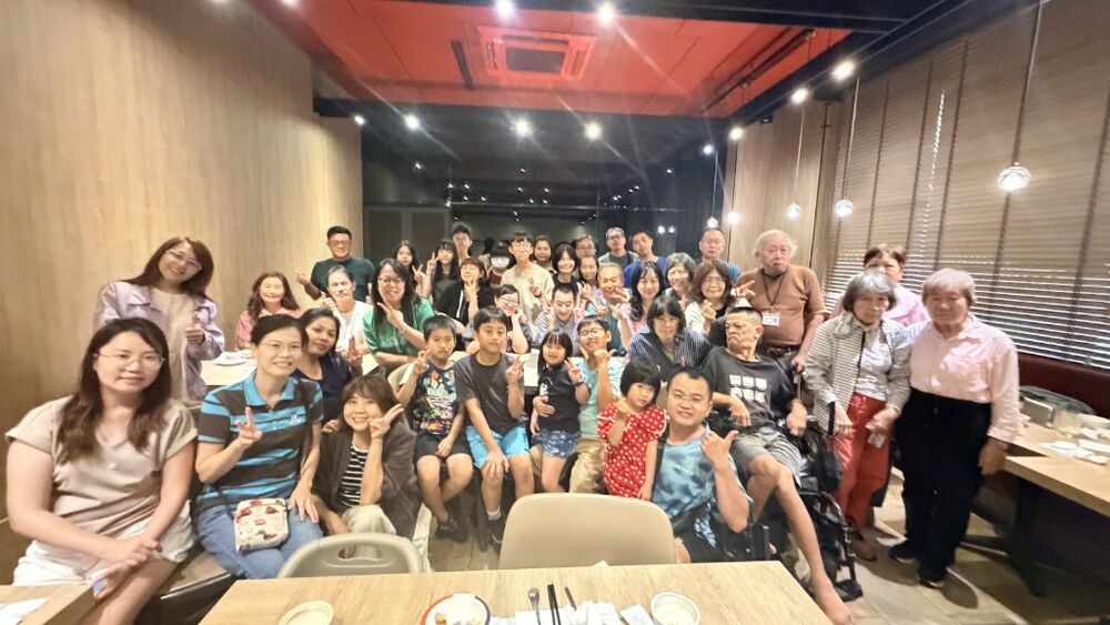 Nearly forty people, from elders to toddlers, posing together around a long table after the service.