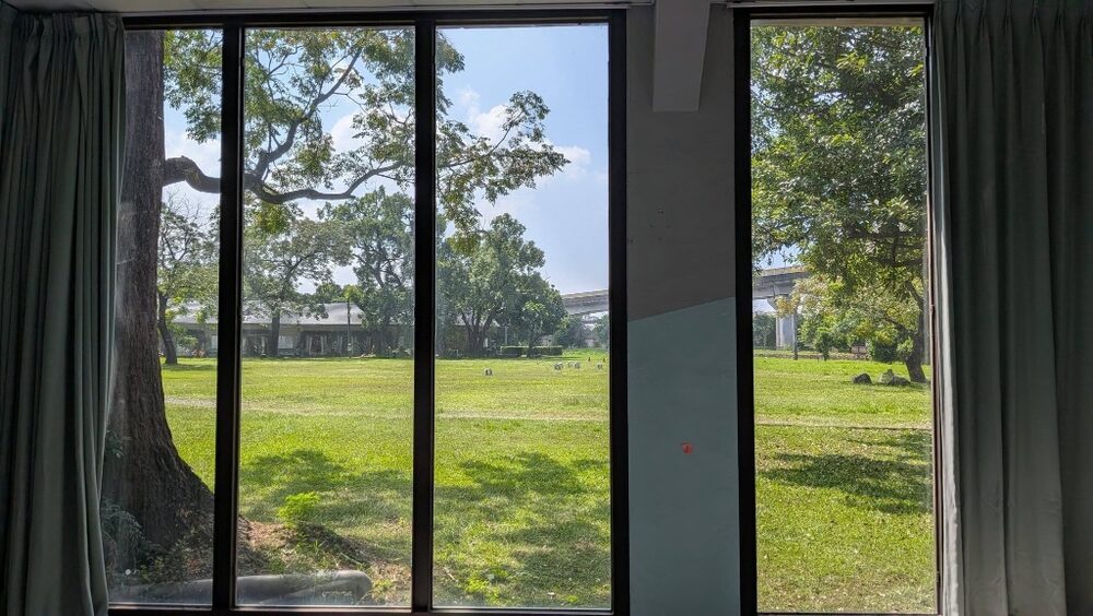 The view from the church’s floor-to-ceiling windows: open lawn and old trees in the sugar refinery grounds, with an elevated MRT line in the distance.