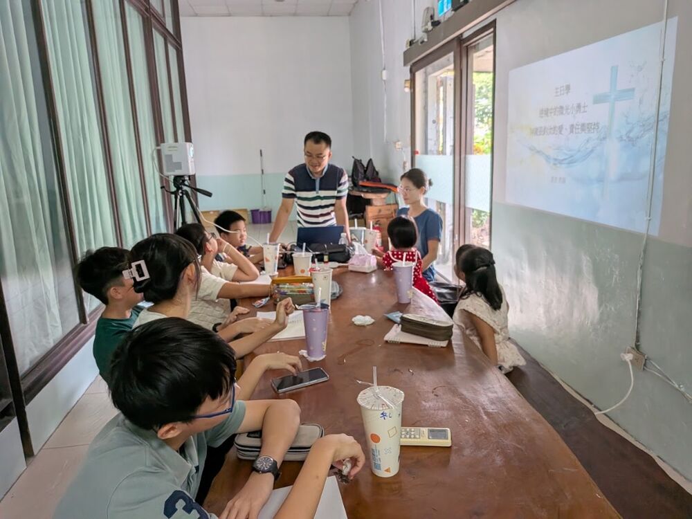 Children gathered around a long table; the screen shows the Sunday school theme.