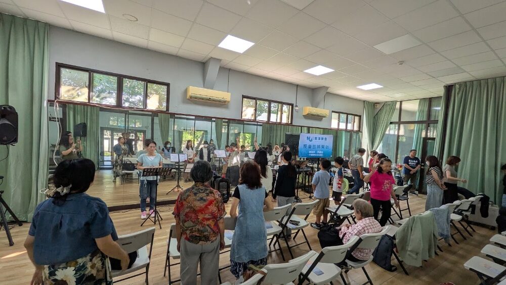 The congregation standing in worship in front of folding chairs, with a projection screen and instruments at the front.